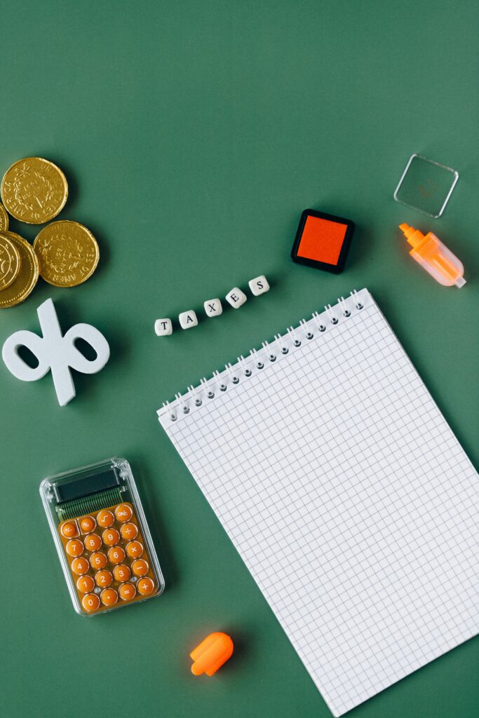 Calculator, coins, notepad and tax-related items arranged on a green background to illustrate tax and inheritance tax planning.