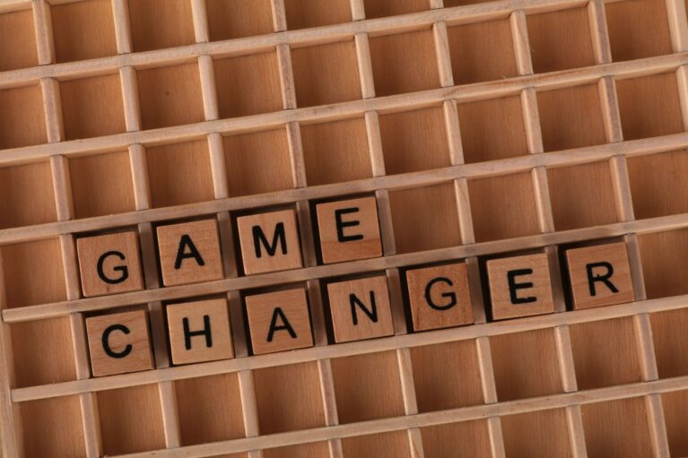 Wooden letter tiles spelling “game changer” in a compartmented wooden tray.
