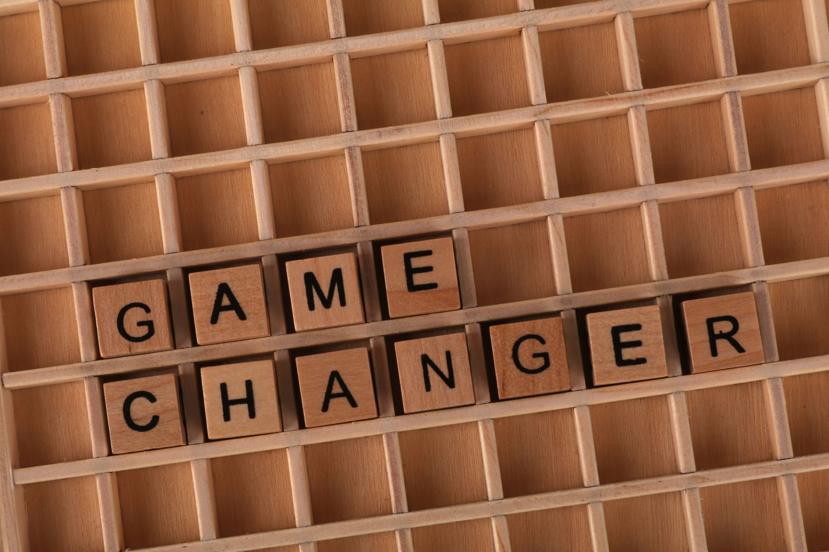 Wooden letter tiles spelling “game changer” in a compartmented wooden tray.