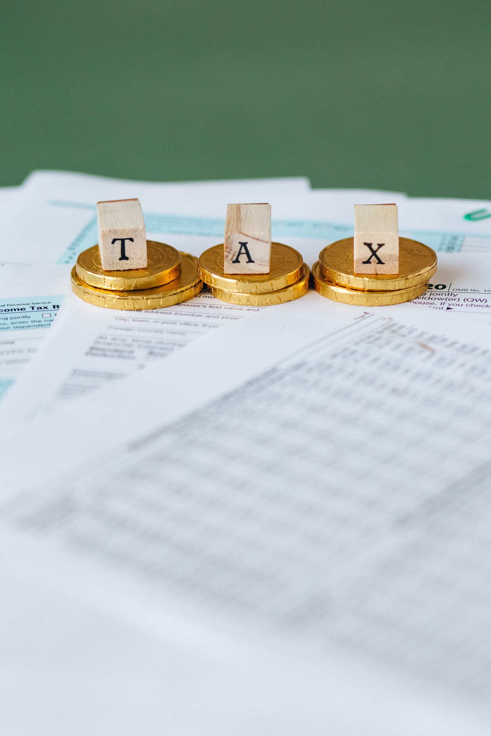 Gold coins and tiles spelling TAX on financial documents.